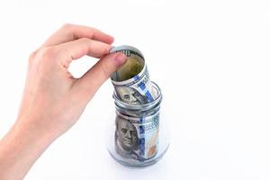 Hand folds paper American one hundred dollar bills, money in a glass jar. Concept for making deposits, saving money. White background. Copy space. photo