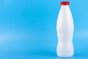 White plastic bottle with red cap for milk on a blue background. Copy space. photo