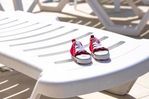 A pair of red sneakers for a boy on a white sun lounger by the pool. Travel concept with children, childish lifestyle. Copy space. photo