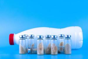 Vials, ampoules with dry probiotic, bifidobacteria and a bottle with milk on a blue background. Copy space. photo