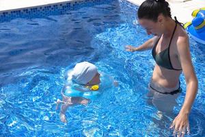 Young mother, a beautiful girl and a child in a children's inflatable circle, in a blue pool on vacation. photo