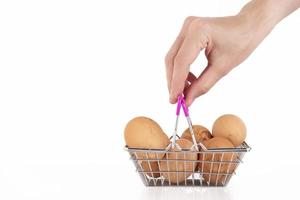 una mano femenina sostiene huevos de pollo salvajes beige en una cesta de compras sobre un fondo blanco. enfoque selectivo. copie el espacio foto