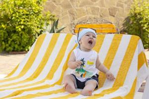 Handsome little boy in sunglasses and a bandana sits on a sun lounger by the pool. Selective focus. photo