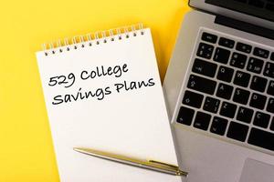 Text, 529 College Savings Plans, Education Loan, written in a notebook lying on a desk with a notebook on a yellow background. photo