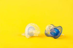 Two baby silicone pacifiers white and blue, on a yellow background. Copy space photo