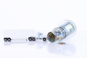 Glass jar full of 100 dollar bills lying sideways and a lorry isolated on white. Copy space. photo