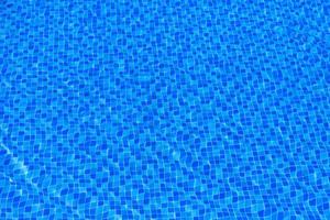 Water ripples on blue tiled swimming pool background. Blue turquoise pool water. Ripples lit up by the sun. Tiles visible below. Top view photo