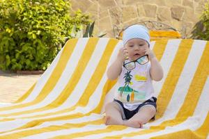 Handsome little boy in sunglasses and a bandana sits on a sun lounger by the pool. Selective focus. photo