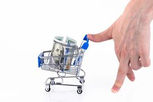 A hand in the form of a walking man rolls up a shopping cart with a roll of one hundred dollar bills. Copy space. photo