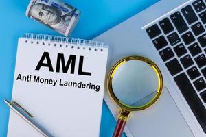 Conceptual image of business acronym AML Anti Money Laundering, written in a notebook lying on a table with a laptop. photo