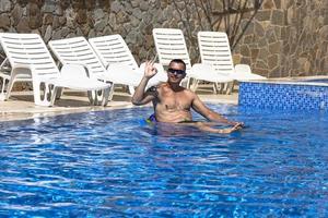 un joven apuesto en la piscina con agua azul se relaja en un día soleado. foto