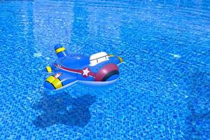 Water ripple on blue tiled pool background. Turquoise water with a floating children's inflatable ring in the form of an airplane. copy space photo