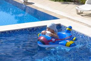 .A child is floating in an inflatable rubber circle in the form of an airplane. A child in an outdoor pool with blue water, photo