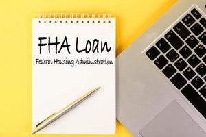 FHA loan from the Federal Housing Administration, the text is written in a notebook lying on a table with a laptop on a yellow background. photo