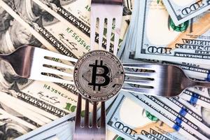 Platinum bitcoin on the background of one hundred dollar bills and cutlery. photo