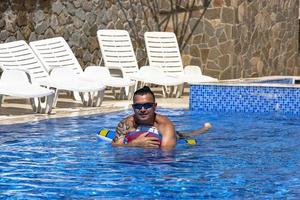 joven apuesto con un anillo inflable en forma de avión en una piscina con agua azul en un día soleado foto