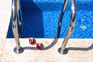 Metal chrome railings, pool ladder for safe entry into the water, and red kids shoes. photo