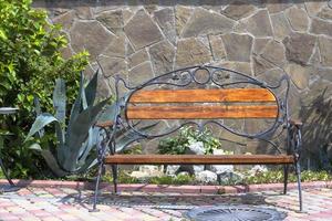 Empty wooden bench on a sunny summer day with a cactus on the background of a stone wall. Mediterranean style. photo