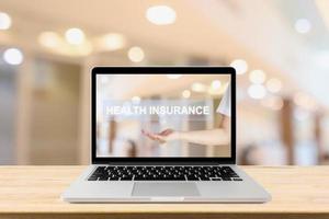 Laptop computer on wood table with female doctor showing Health Insurance text on screen with blur hospital room background healthcare concept photo