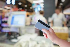 Hand hold credit card with Supermarket cashier checkout counter with customer defocused blur background photo