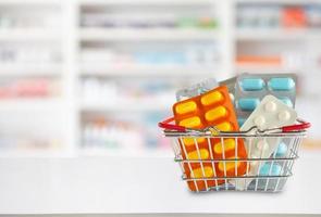 Medicine pills package in shopping basket with pharmacy drugstore shelves blur background photo