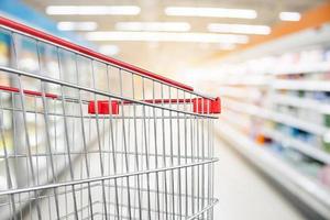 Supermarket aisle blur defocused background with empty red shopping cart photo