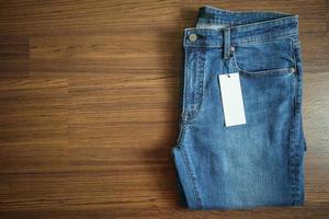 Blue jeans with blank white price label tag on wooden background photo