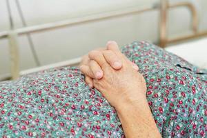 Asian elder senior woman patient holding bed rail while lie down with hope waiting her family in hospital. photo