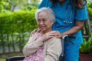 Doctor help Asian elderly woman disability patient sitting on wheelchair in park, medical concept. photo