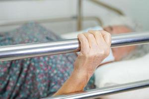 anciana asiática anciana paciente sosteniendo barandilla de la cama mientras se acuesta con esperanza esperando a su familia en el hospital. foto