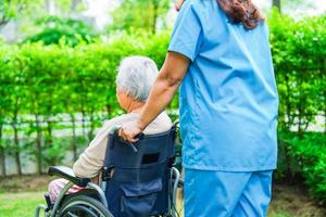 Caregiver help Asian elderly woman disability patient sitting on wheelchair in park, medical concept. photo