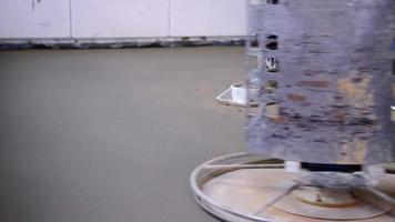 Stampfen und Schleifen von halbtrockenem Estrich durch eine Maschine mit einer rotierenden Scheibe zum Nivellieren. Bau eines Betonbodens im Haus, ein Meister mit Spezialausrüstung. Zeitlupe video