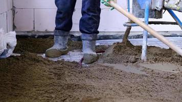 Semi-dry floor screed - a worker shovels a construction mixture through a special sleeve for cementing and leveling on underfloor heating pipes. Slow Motion video