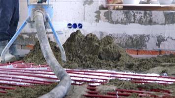 Semi-dry floor screed - a worker shovels a construction mixture through a special sleeve for cementing and leveling on underfloor heating pipes. Slow Motion video