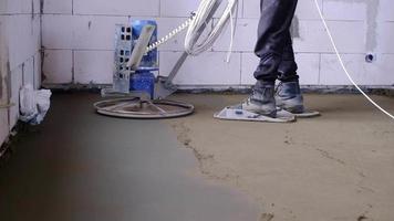 Ramming and grinding of semi-dry floor screed by a machine with a rotating disk for leveling. Construction of a concrete floor in the house, a master with special equipment. Slow motion video