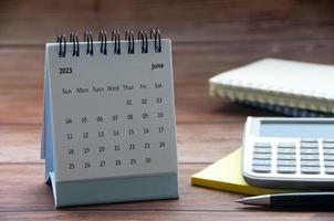 June 2023 white desk calendar on wooden table with notepad, calculator and pen background. Copy space photo