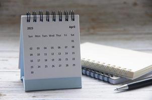 abril de 2023 calendario de escritorio blanco sobre mesa de madera con bloc de notas y fondo de pluma. concepto de calendario y espacio de copia foto