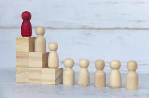 Wooden people figures on top of wooden blocks with red figure leading the rest. Business concept photo