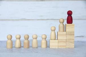 Wooden people figures on top of wooden blocks with red figure leading the rest. Business concept photo