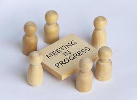 Wooden people figures having business meeting with meeting in progress text on wooden table. photo