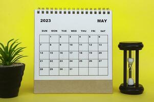 May 2023 desk calendar with table plant and minutes glass on yellow background. photo