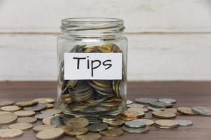 Tips label on coin jar on top of wooden desk with asorted coins background. photo