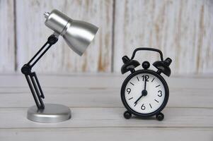 Alarm clock pointing at 7 o'clock with table lamp on wooden background. photo