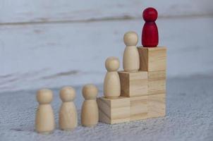 Wooden people figures on top of wooden blocks with red figure leading the rest. Business concept photo