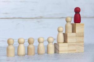 Wooden people figures on top of wooden blocks with red figure leading the rest. Business concept photo