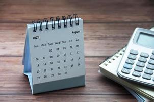 August 2023 white desk calendar on wooden table with notepad and calculator background. photo