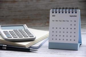 September 2023 white desk calendar on wooden table with notepad and calculator background. Business concept photo