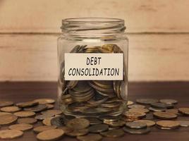 Debt consolidation label on coin jar on top of wooden desk with asorted coins background. photo