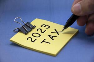 Tax 2023 text written on yellow notepad on blue cover background. photo