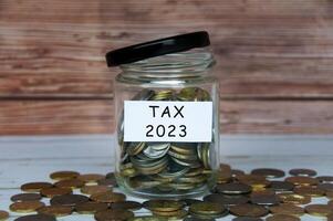 Tax 2023 label on coin jar with scattered coins on wooden table. photo